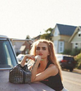 A woman leaning on the hood of her car.