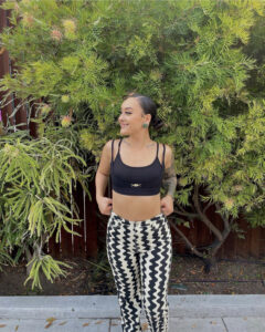 A woman in black and white pants standing next to a tree.