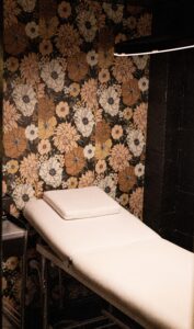 A white massage table in front of a floral wall.