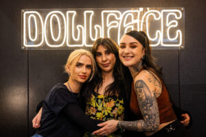 Three women posing for a picture in front of a neon sign.