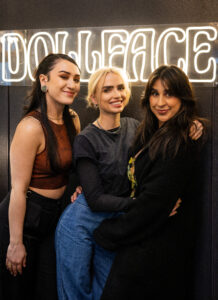 Three women posing for a picture in front of a neon sign.