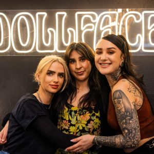 Three women posing for a picture in front of a neon sign.